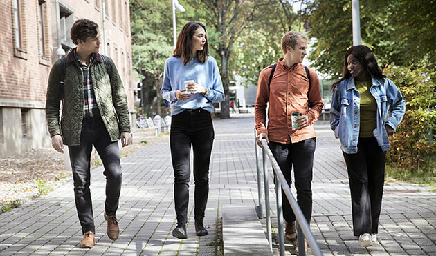 Fyra studenter går utanför universitetsbyggnad. Foto.