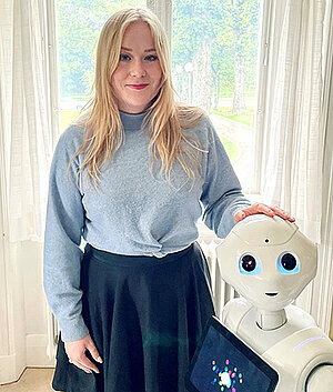 Julia Rosén står bredvid en robot. Foto.