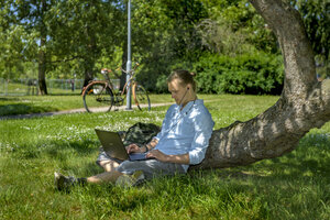 En manligt kodad student sitter i en park med en bärbar dator i knäet. Det är sommar. 